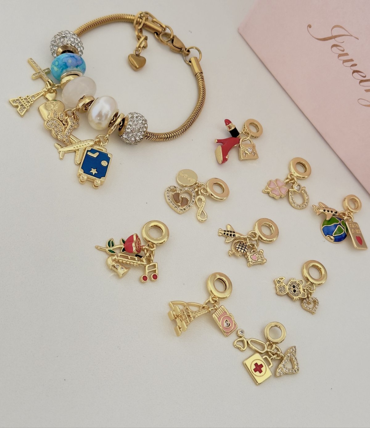 Charms disponibles en dorado: torre Eiffel, cámara, gatito, huellita, botiquín, rosa, avión, maleta, trébol y más