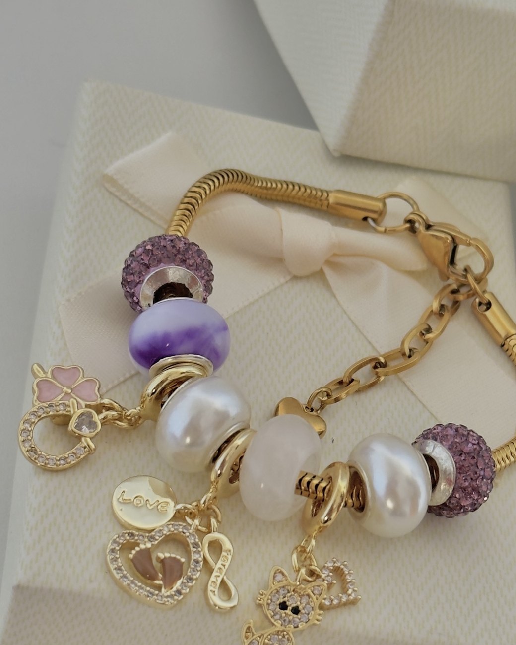 Pulsera dorada con cuentas lila, perlas, cuarzo y charms de trébol, corazón, infinito y gatito